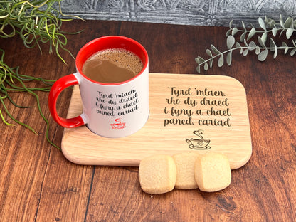 A red and white mug with a message on it, placed on a wooden tray with cookies, and some greenery in the background.