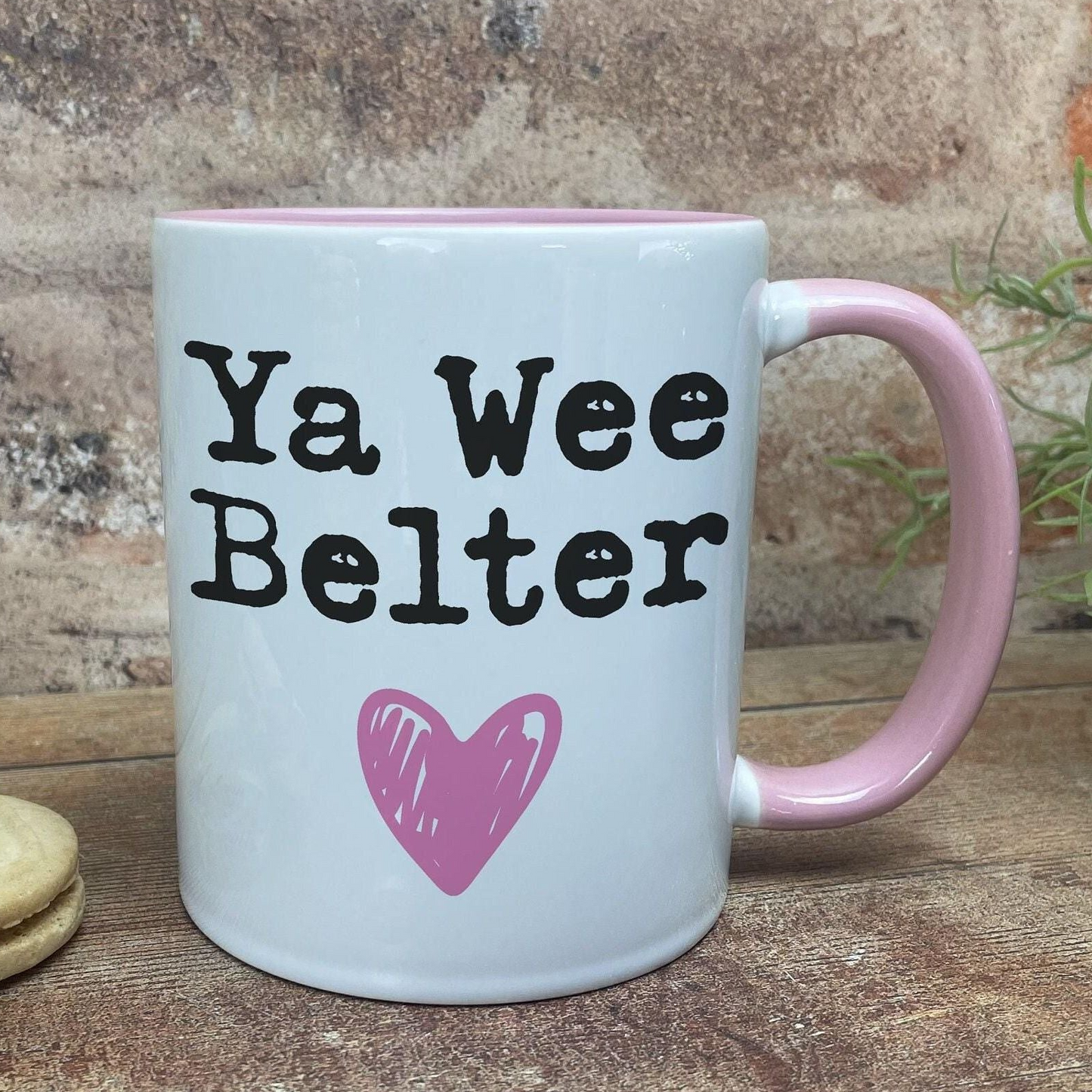 A white mug with a pink handle, featuring the text "Ya Wee Belter" and a pink heart symbol.