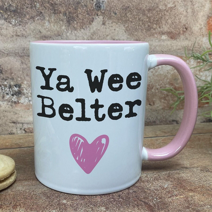 A white mug with a pink handle, featuring the text "Ya Wee Belter" and a pink heart symbol.