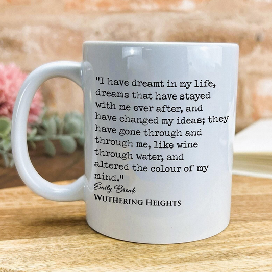 A white ceramic mug with a quote from the novel "Wuthering Heights" printed on it, placed on a wooden surface.
