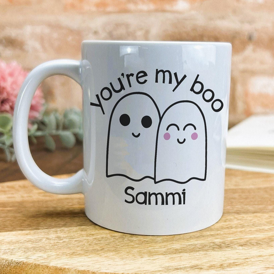 A white mug with a humorous text and cartoon-style ghost characters printed on it.
