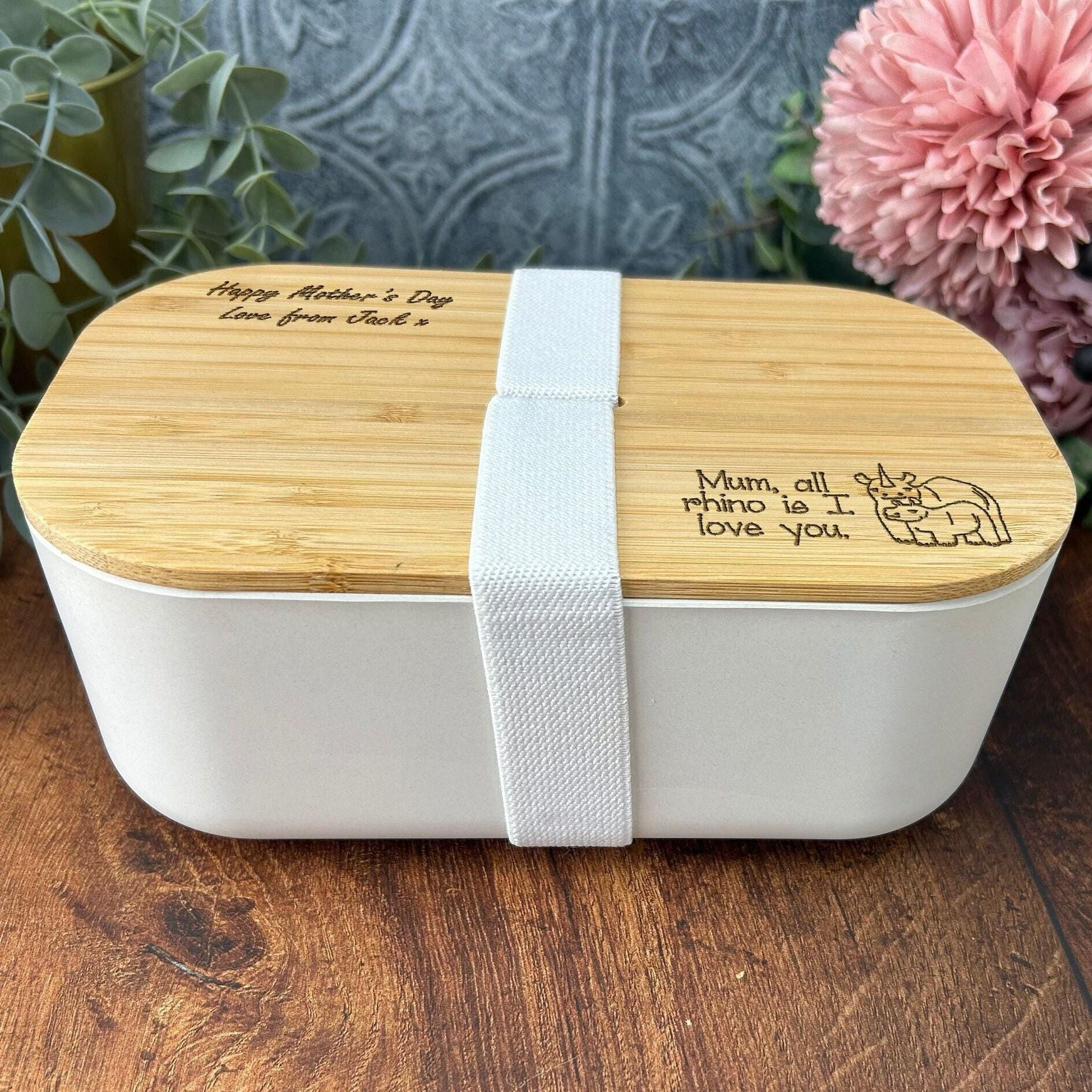 A white bento box with a wooden lid, featuring a personalized message engraved on it.