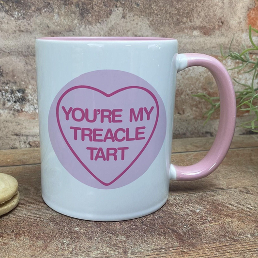 A white mug with a pink handle, featuring a heart-shaped design with the text "YOU'RE MY TREACLE TART" printed on it.
