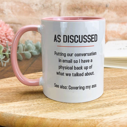 a pink and white coffee mug sitting on top of a wooden table