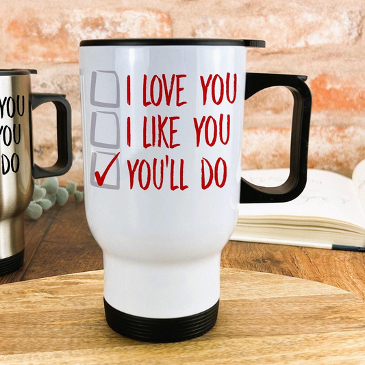 A white travel mug with red text that says "I LOVE YOU I LIKE YOU YOU'LL DO" on it, placed on a wooden surface.