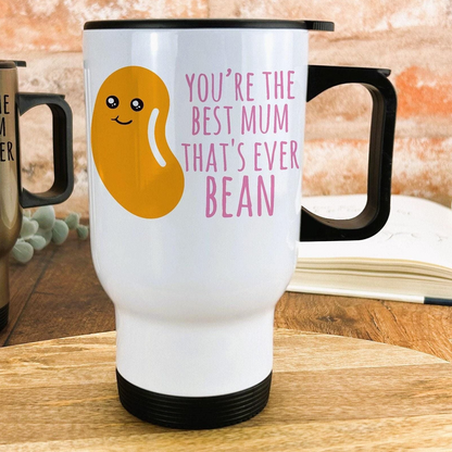 A white travel mug with a black handle, featuring a cartoon bean design and text that reads "You're the best mum that's ever bean".