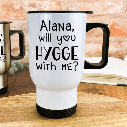 A white travel mug with black text that says "Alana, will you hygge with me?"