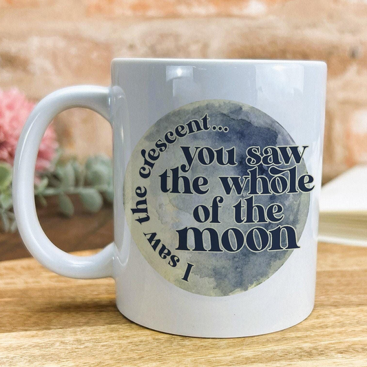 A white ceramic mug with a printed design featuring a moon-like shape and text that reads "The ascent... you saw the whole of the moon".