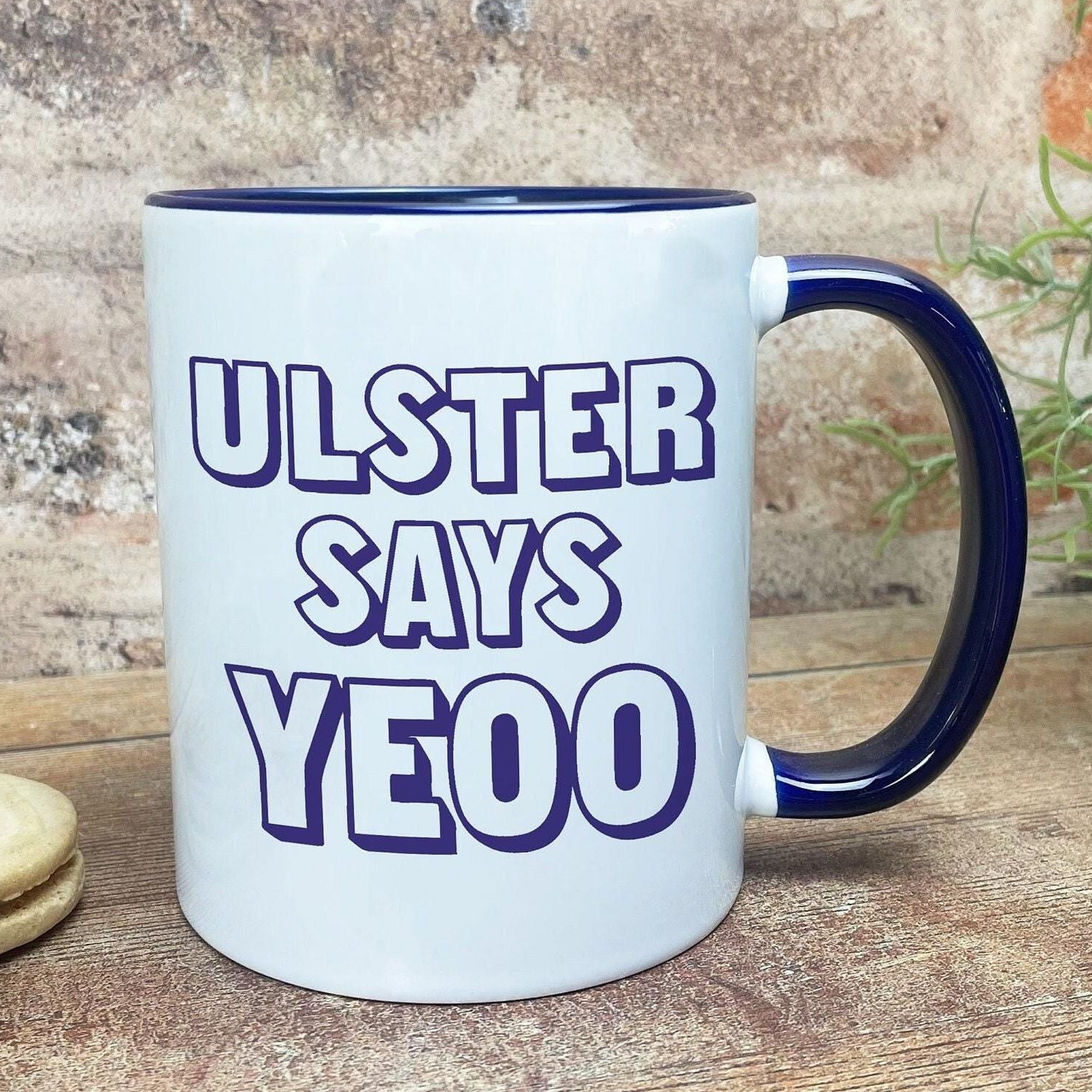 A white mug with a blue handle, featuring the text "ULSTER SAYS YEOO" in a playful, humorous font.