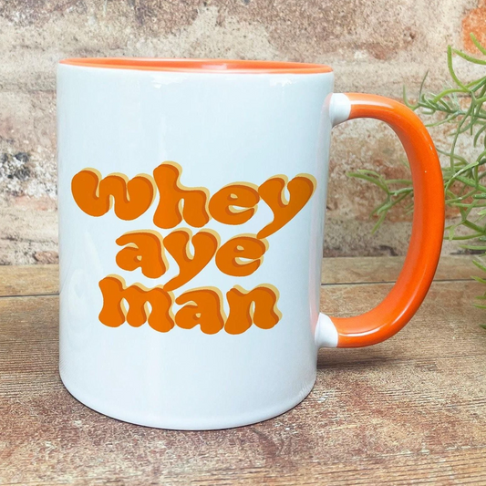 A white mug with an orange handle, featuring the text "whey aye man" in a retro style.