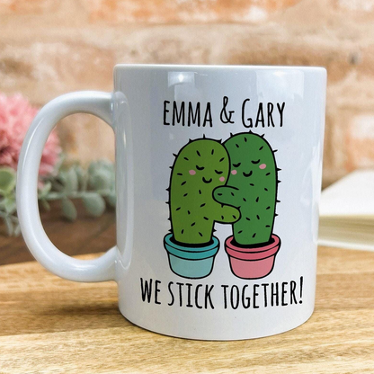 A white ceramic mug with a printed design featuring two cacti hugging each other, accompanied by the text "Emma & Gary We stick together!"