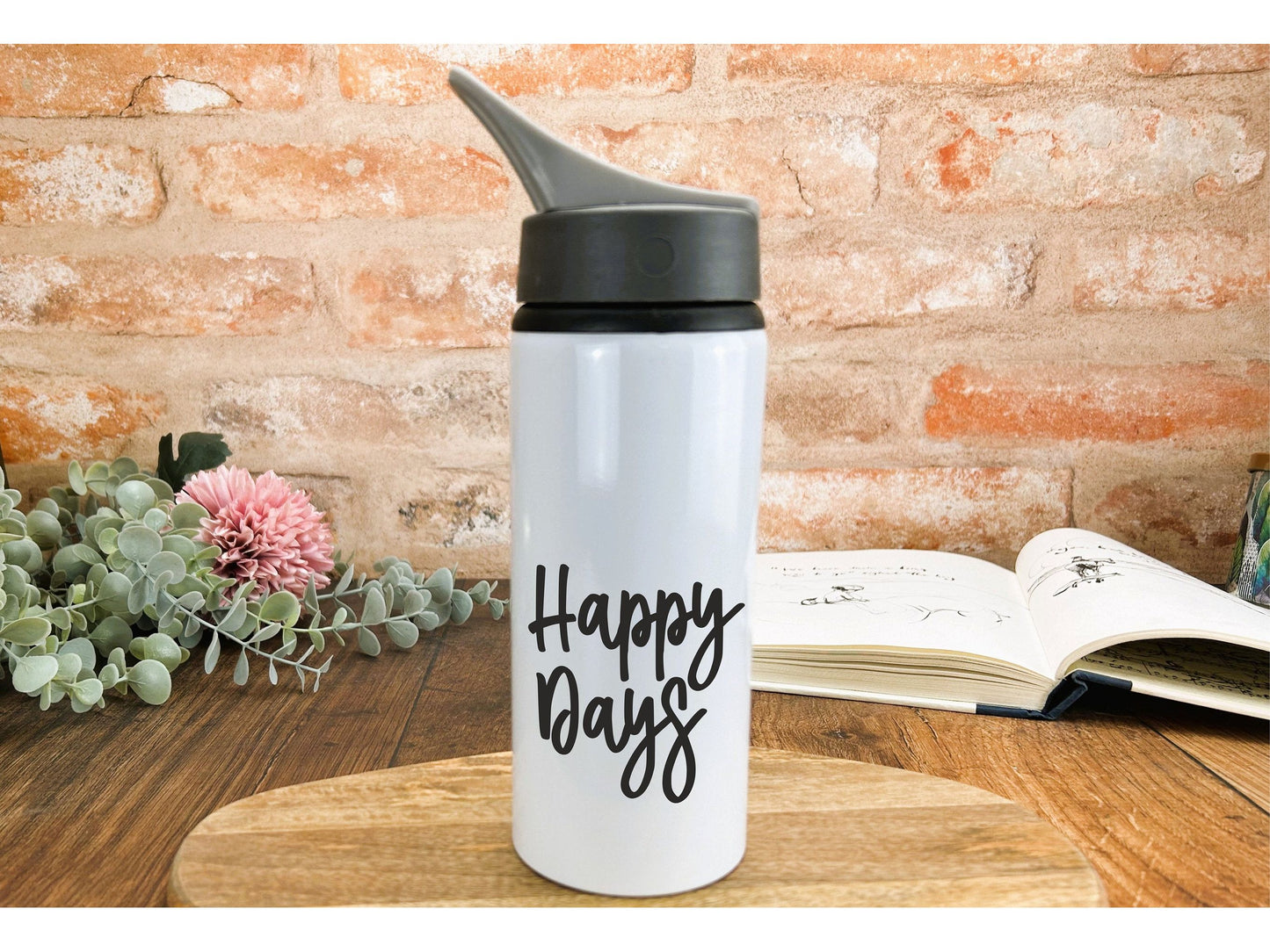 a happy bag water bottle sitting on a table next to an open book