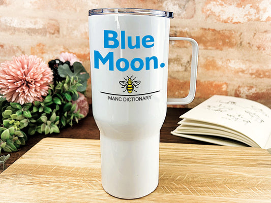 a blue moon travel mug sitting on a table next to a book